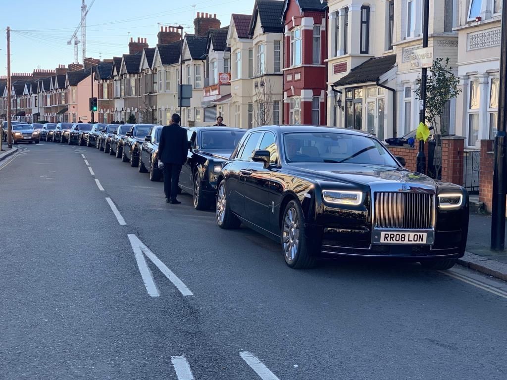 Row of luxury black cars parked along a residential street with Victorian-style houses.