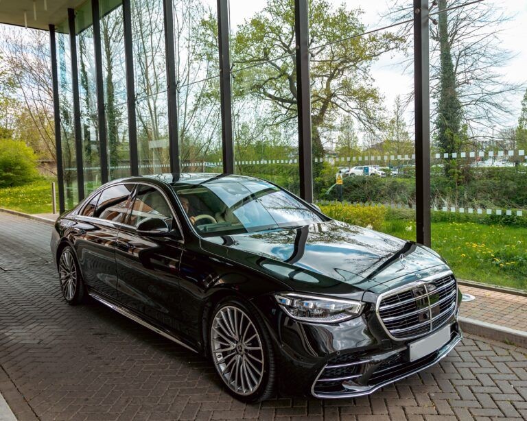 Black luxury car parked in front of large glass windows with greenery outside.